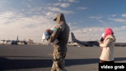 Казахстанский военный несет ребенка во время гуманитарной операции «Жусан». Женщина с детьми возвращается в Казахстан. 