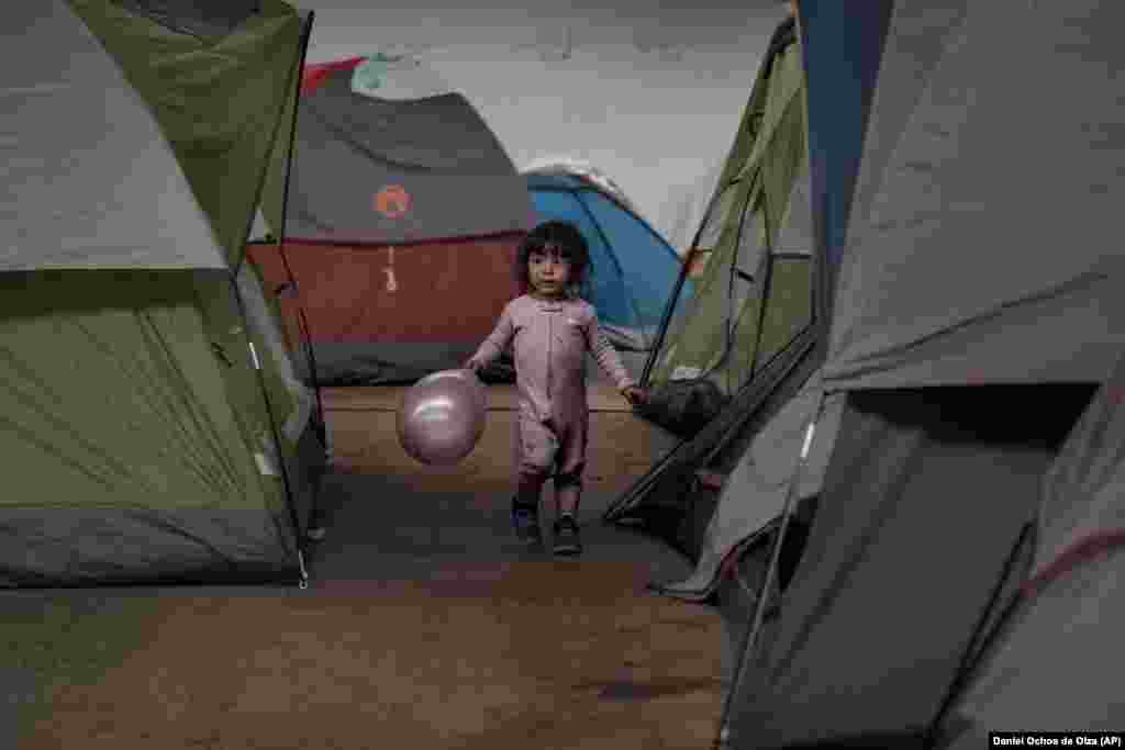 A girl holds a balloon as she walks among tents inside an empty warehouse used as a shelter set up for migrants in downtown Tijuana, Mexico. (AP/Daniel Ochoa de Olza)