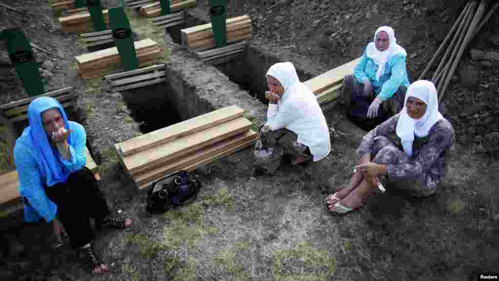 Muslim women sit near a new open grave prepared for the coffin of their relative on July 10.