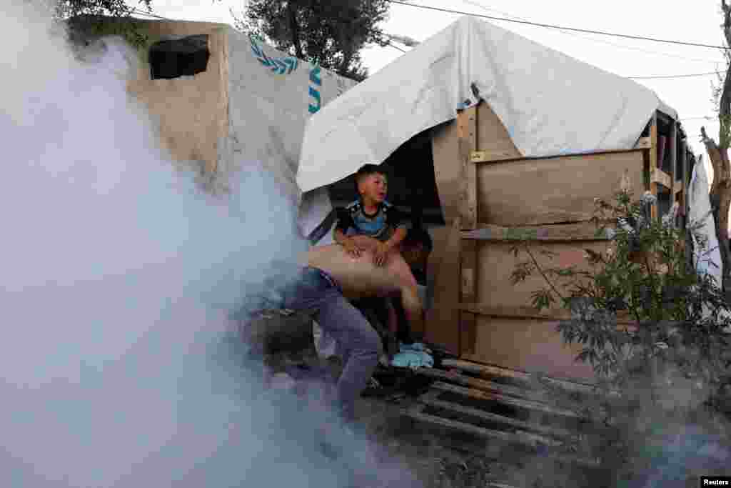 Një migrant mban një fëmijë, teksa ikin nga gazi lotësjellës i hedhur nga policia. Protestat e dhunshme janë të shpeshta në kampet e migrantëve në Greqi. 