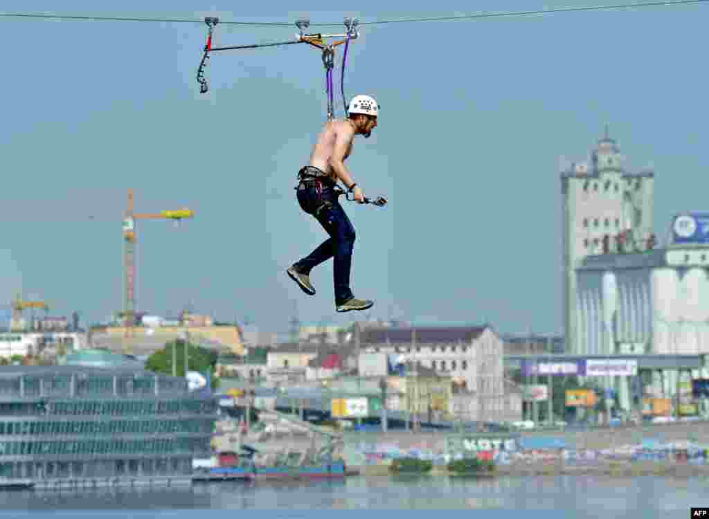 A man hanging by his skin crosses the Dnipro River on a 552-meter-long cable between the two banks of the water in Kyiv on May 23. (AFP/Sergei Supinsky)