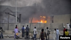 People watch as smoke rises from police headquarters after they were hit by a blast in Nigeria's northern city of Kano on January 20. 