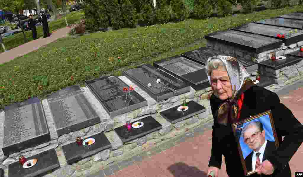A widow carries a portrait of her husband as she walks in front of a gravestone with the names of those who died as a result of the 1986 Chernobyl nuclear catastrophe. A ceremony at a Chernobyl memorial in Kyiv on April 26 marked the 31st anniversary of the world's worst civilian nuclear accident. (AFP/Sergei Supinsky)