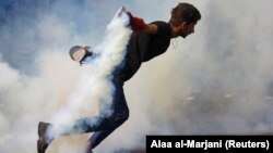 An Iraqi demonstrator runs as he carries a tear-gas canister during ongoing anti-government protests in Baghdad, November 14, 2019
