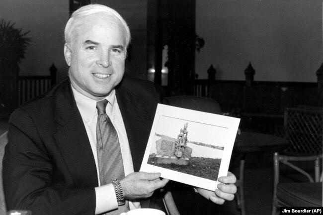 Джон Маккейн с фотографией монумента, который возведен во Вьетнаме в честь его пленения, 18 февраля 1985