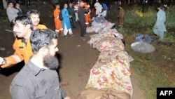 Pakistani rescue workers stand next to the covered remains of victims at the crash site.