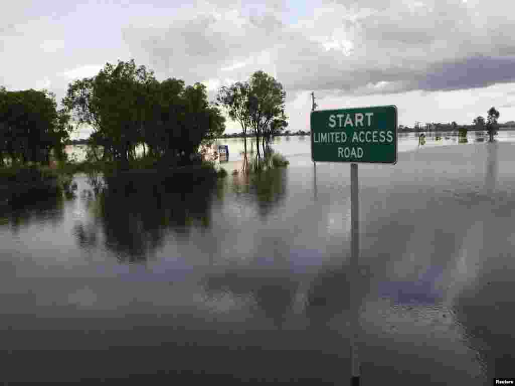 A street sign is seen partially covered by floodwaters, 6 km (3.7 miles) south of Rockhampton, January 3, 2011. Military aircraft flew supplies to an Australian town slowly disappearing beneath floodwaters on Monday, as record flooding in the country's northeast continues to cut coal exports and devastate wheat production. REUTERS/Daniel Munoz (AUSTRALIA - Tags: DISASTER ENVIRONMENT 