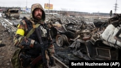 Защитник Украины возле уничтоженной российской военной техники в городе Буча неподалеку от Киева, 1 марта 2022 года