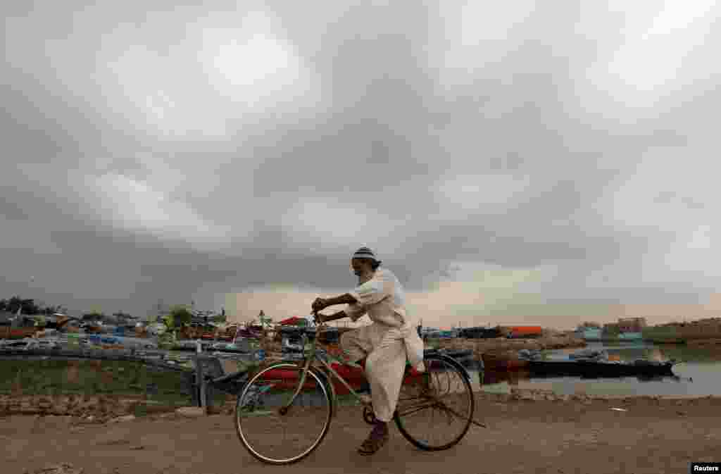 An elderly man rides a bicycle past fishing boats with monsoon clouds looming in Karachi on July 19. (Reuters/Akhtar Soomro)