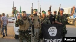 Shi'ite fighters pose with a black flag belonging to the Islamic State, which they pulled down after capturing the town of Jurf al-Sakhar from the Islamist militants on October 26.