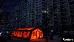 Намет державного пункту гуманітарної допомоги, де мешканці можуть зігрітися, зарядити свої пристрої, отримати гарячі напої і психологічну підтримку, встановлений перед багатоквартирним будинком під час відключення електроенергії, Київ, 12 січня 2026 року