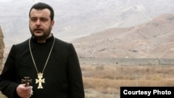 Iran -- An Armenian priest prays on the Iranian-Azerbaijani border against the backdrop of Azerbaijani soldiers destroying Armenian cross stones at the Djulfa cemetery, December 2005. (Photo couresty of Djulfa.com)