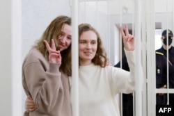 Katsyaryna Andreyeva (right) and Daryya Chultsova flash victory signs from the defendant's cage during their trial in Minsk on February 18.