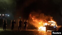 Pjesëtarët e policisë përballen me protestuesit pranë një makine policie të djegur pas një sulmi me thikë në afërsi të një shkolle në Dublin. Irlandë, 23 nëntor 2023.