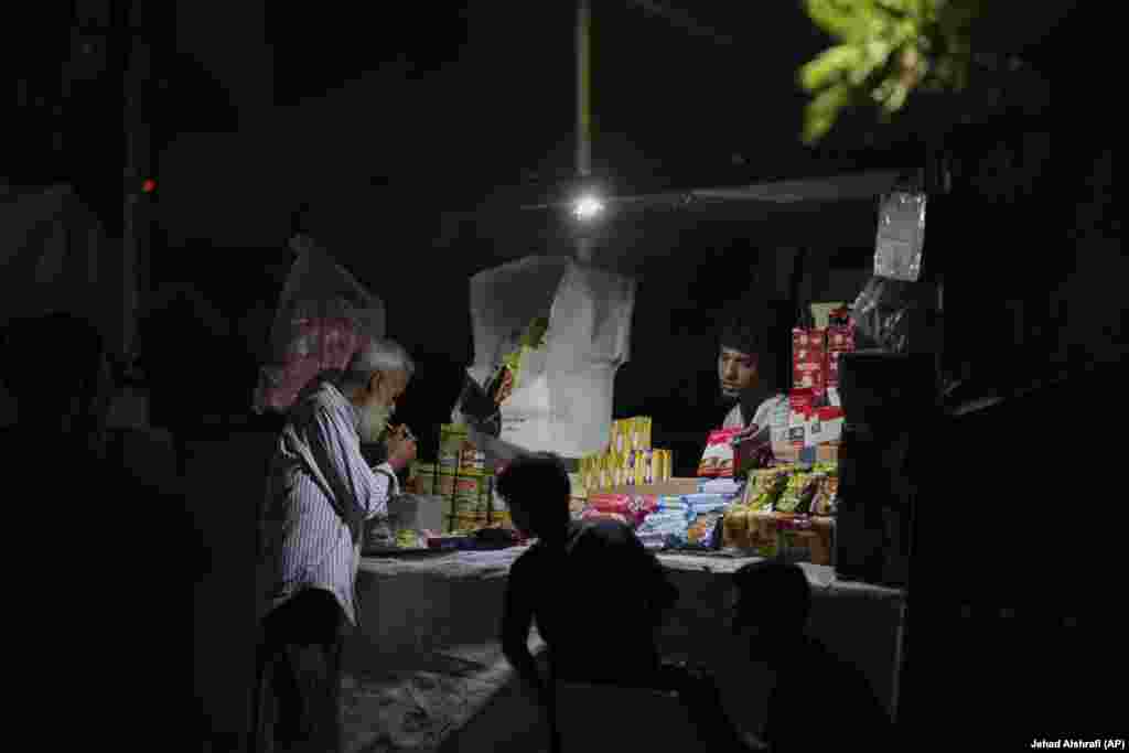 Një burrë palestinez duke ndezur një cigare, teksa një shitës ambulant shikonte tezgën e tij pranë plazhit.