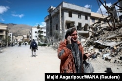 A woman talks on her phone in a residential Tehran neighborhood that was damaged in an air strike in March.