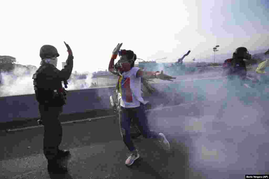 An opponent of Venezuelan President Nicolas Maduro high fives a rebel soldier on a highway overpass outside La Carlota air base amid tear gas fired by loyalist troops inside the base in Caracas on April 30. (AP/Boris Vergara)