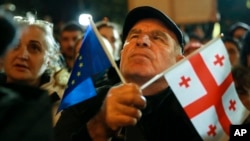 A demonstrator holds an EU and a Georgian national flag as he attends an opposition protest against the results of the parliamentary elections in Tbilisi on October 28.