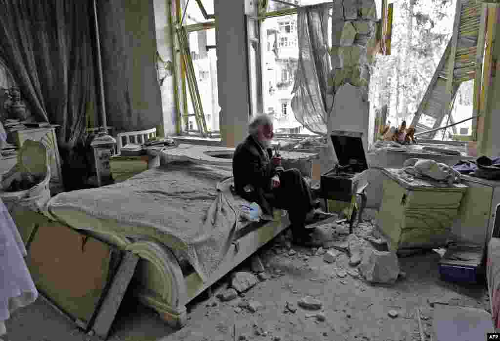 Mohammad Mohiedine Anis, 70, smokes his pipe as he sits in his destroyed bedroom listening to music on his vinyl player in Aleppo&#39;s formerly rebel-held Al-Shaar neighborhood. (AFP/Joseph Eid)