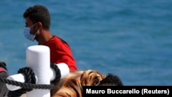Migránsok pihennek egy mentőhajó fedélzetén Lampedusa partjainál 2021. május 9-én