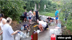 Жителі Маріуполя набирають воду з джерела у приватному секторі в Іллічевському (після декомунізації Кальміуському) районі міста. Рутуб-канал «Мариуполь. Так и живём», 5 серпня 2026 року