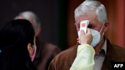 Egy boszniai egészségügyi alkalmazott egy oltópontra érkező férfi testhőmérsékletét méri. 