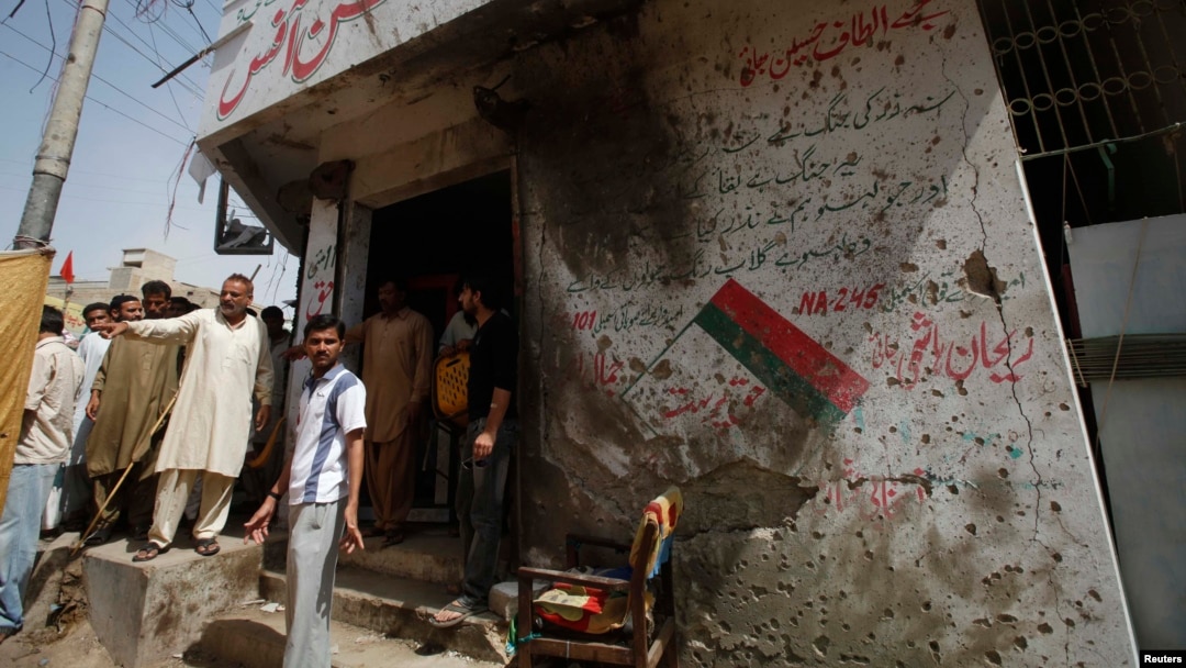 Men stand outside the campaign offices of the Muttahida Qaumi Movement (MQM) political party in Karachi on April 26, after a bomb blast.