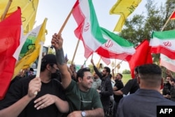 People wave flags near the Iranian Embassy in Baghdad on June 15 during celebrations following the announcement of a deal to end the war between Iran and the United States.