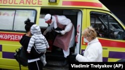 Медик в защитном костюме выходит из машины скорой помощи. 