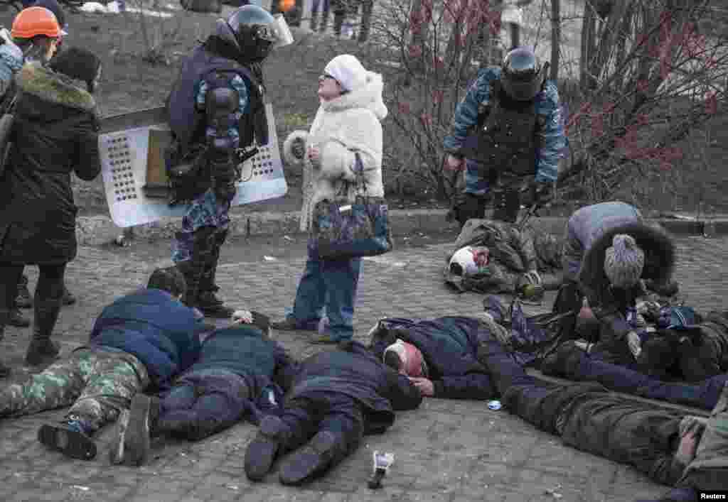 Riot police stand near people wounded during clashes.