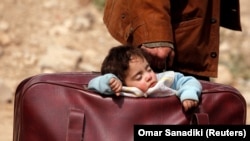 A Syrian child sleeps in a bag in the village of Beit Sawa, eastern Ghouta, as his family flees the area on March 15, 2018.