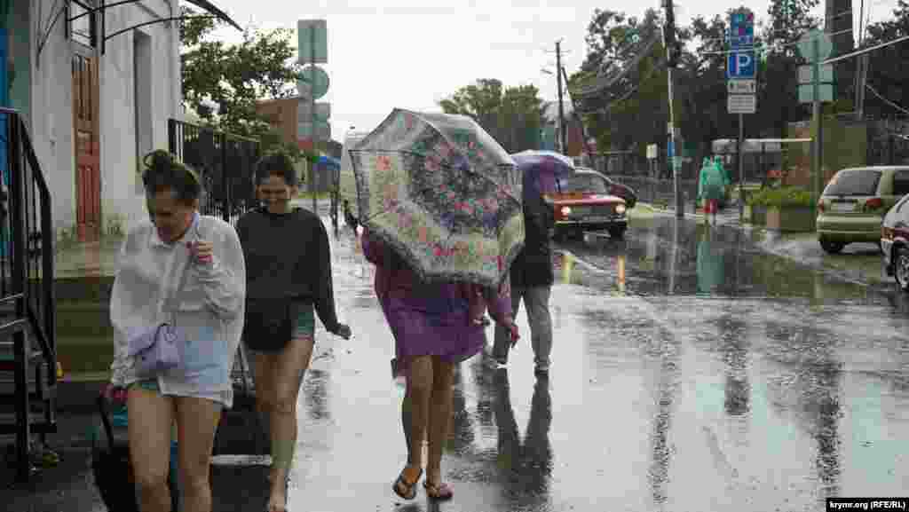 Люди пытаются укрыться от ливня под зонтом