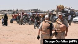 Russian and Syrian forces stand guard as civilians enter a crossing into Idlib Province.