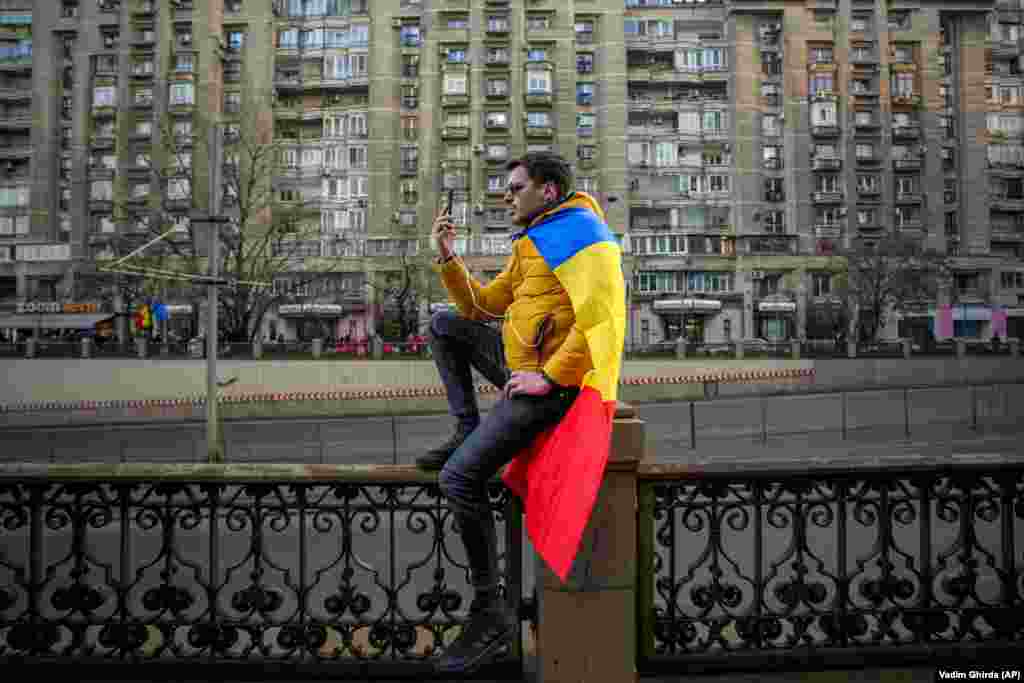 A man draped in a Romanian flag takes a video with his phone during a rally protesting the annulment of the first round of presidential elections by Romania&#39;s Constitutional Court in December.&nbsp;