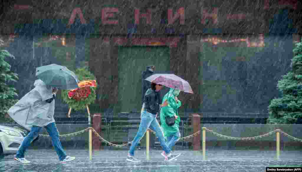 Këmbësorët mbrohen nga një stuhi shiu derisa ecin pranë mauzoleut të themeluesit të Shtetit sovjetik Vladimir Lenin, në Sheshin e Kuq, në Moskë, më 30 qershor.