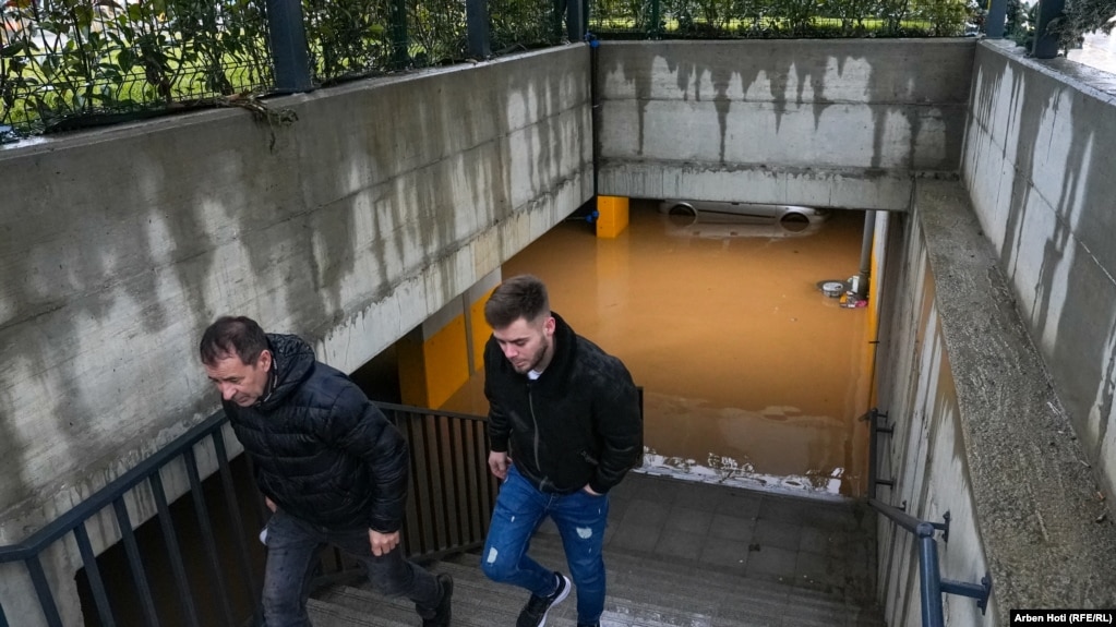 Dy persona duke ngjitur disa shkallë, teksa prapa tyre shihet niveli i lartë i ujit që është grumbulluar pas vërshimeve.