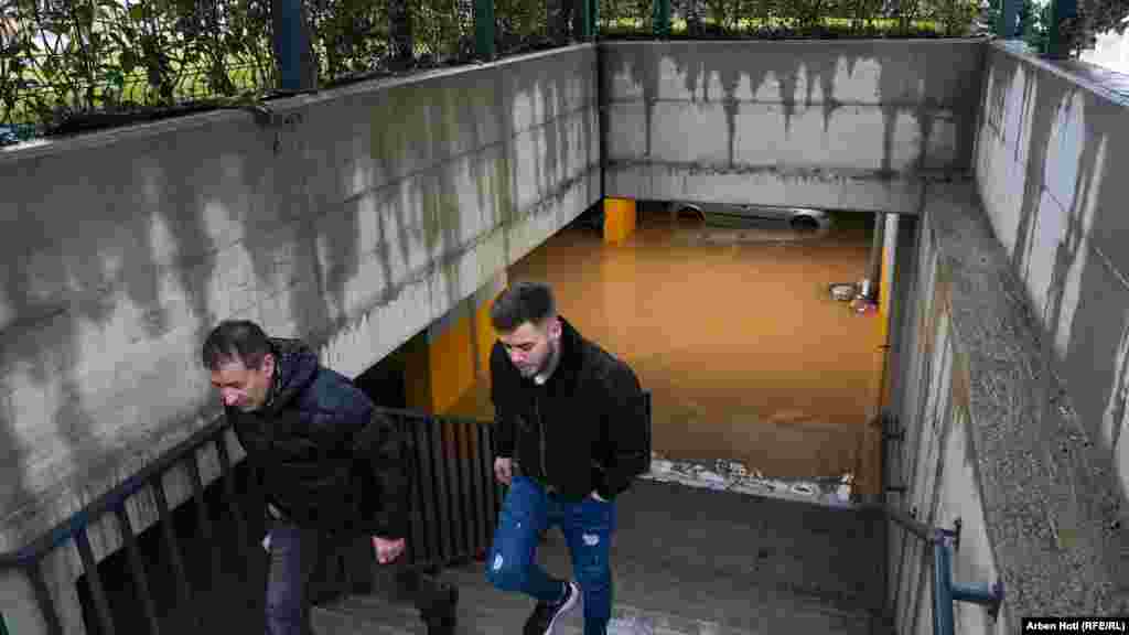 Dva čovjeka penju se uz stepenice, dok se iza njih vidi velika količina vode koja se zadržala nakon poplava.