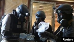 A UN chemical weapons expert, wearing a gas mask, holds a plastic bag containing samples from one of the sites of an alleged chemical weapons attack in the Ain Tarma neighbourhood of Damascus last August. 