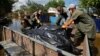 Voluntarii încarcă saci cu cadavre recuperate pe 16 iunie din casele inundate, după ce apele s-au retras în urma ruperii barajului Kahovka