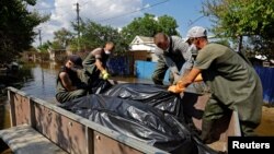 Voluntari și lucrători municipali scot saci cu cadavre din casele inundate, după ce apele s-au retras în urma distrugerii barajului Nova Kakhovka, în orașul Hola Pristan din regiunea Herson, Ucraina controlată de Rusia, 16 iunie 2023.