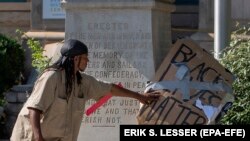 Un protestatar pune o placardă la baza obeliscului Memorialului Confederat în Decatur, Georgia, Statele Unite ale Americii, 12 iunie 2020. 