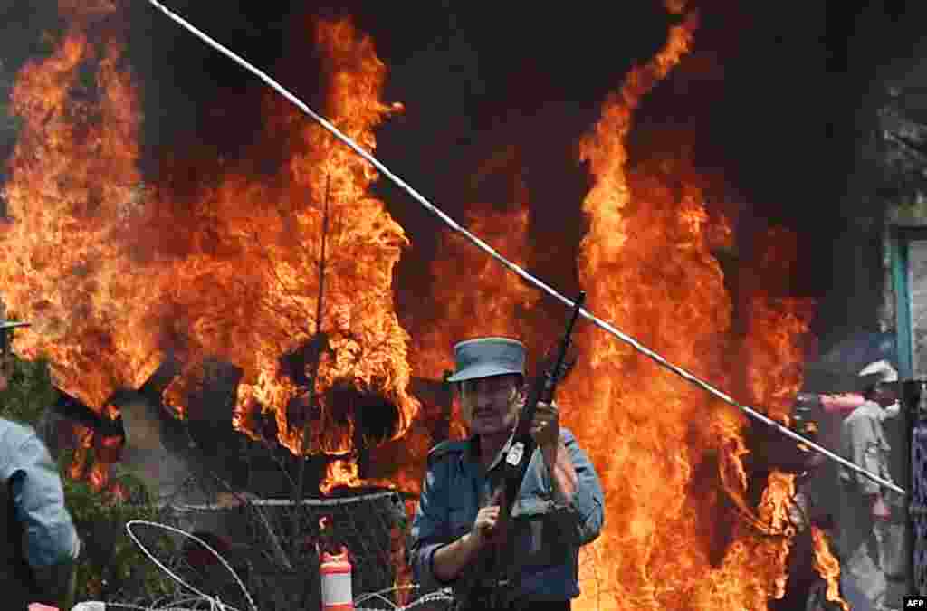 An Afghan policeman stands guard as smoke and flames rise from the site of a huge blast near the entrance to Kabul&#39;s international airport. Afghan Health Ministry spokesman Wahidullah Mayar posted on Twitter that seven civilians, including a child, were killed in the attack. (AFP/Shah Marai)