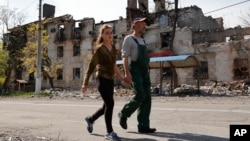 Local residents walk past a destroyed building in the Ukrainian port city of Mariupol on territory currently controlled by Russia-backed forces on April 29. .