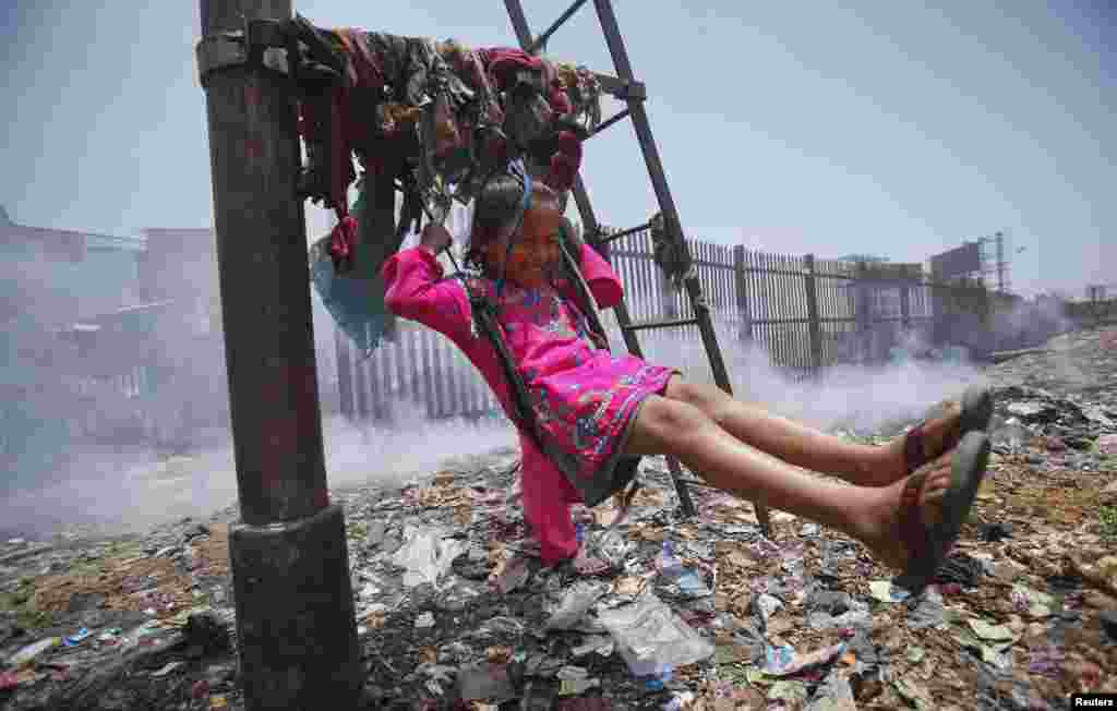 Sana, 5, plays on a cloth sling hanging from a telephone pole as smoke from a garbage dump rises next to a railway track in Mumbai, India.