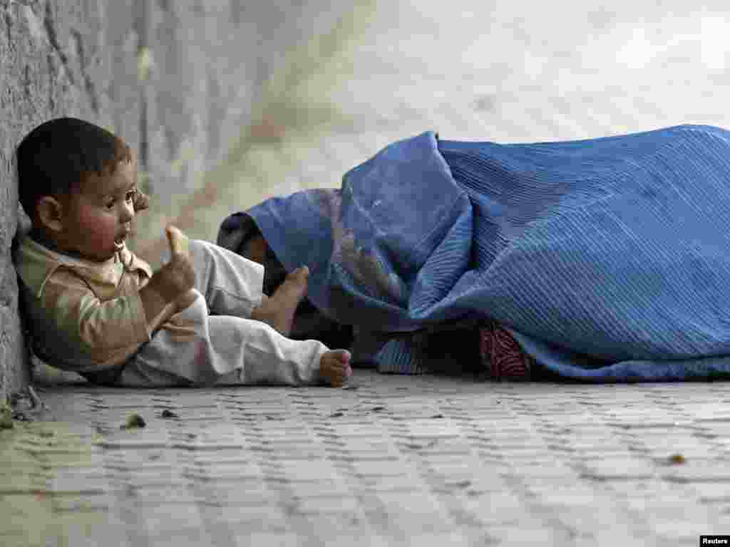 An Afghan woman sleeps by the roadside as her child nibbles a piece of bread outside a mosque during Ramadan in Kabul on September 8. Photo by Fayaz Kabli for Reuters