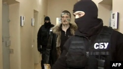 A Russian Channel 1 screen grab shows a man identified as Adam Osmayev (center), one of the suspects alleged to have conspired to kill Vladimir Putin, being escorted by masked agents of the Ukrainian Security Service in Odesa.