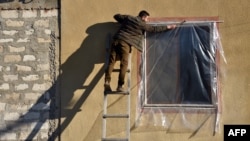 Житель Степанакерта заклеивает разбитое во время бомбежек окно своего дома