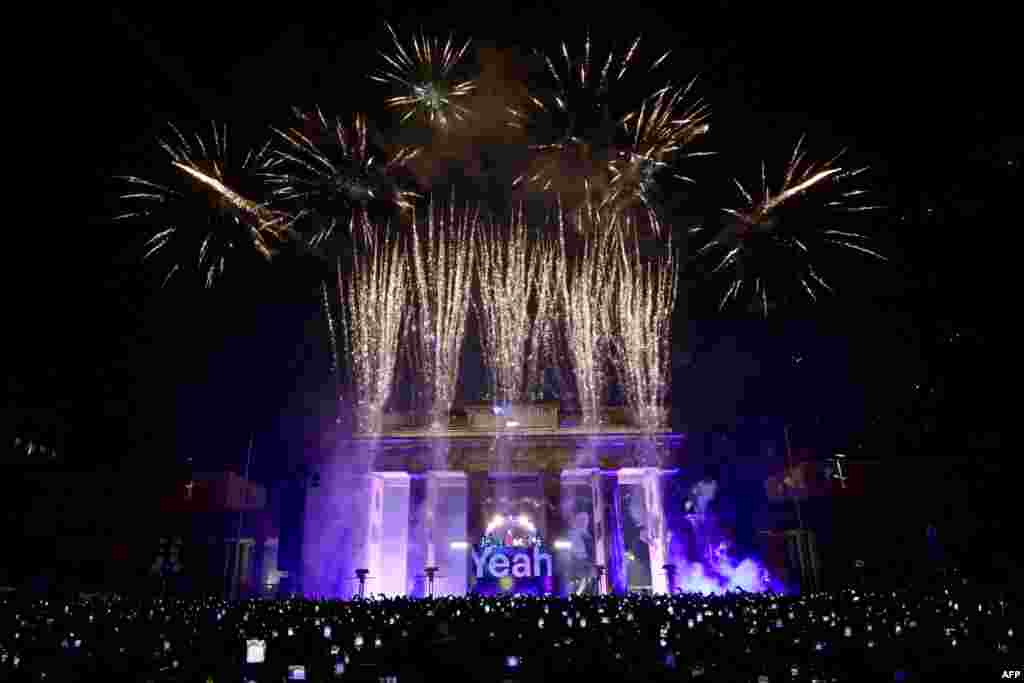 Oamenii filmează și fotografiază cu telefoanele mobile în timp ce artificiile explodează deasupra Poartei Brandenburg, simbolul orașului Berlin, în timpul festivităților intitulate „Yeah 26” pentru a sărbători Anul Nou, la Berlin, pe 1 ianuarie 2026. Fotografie de John MACDOUGALL / AFP