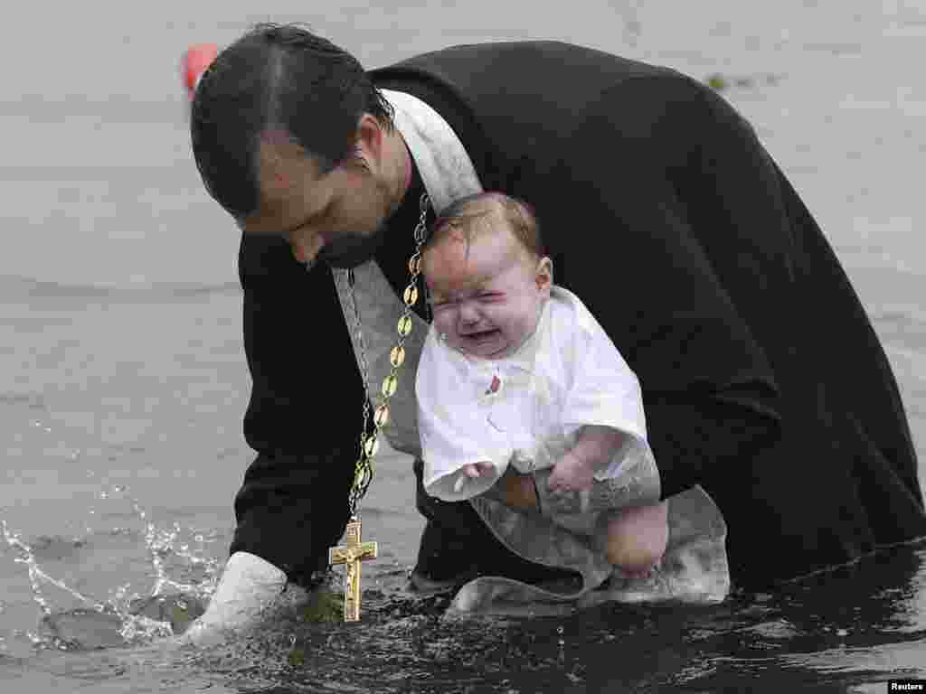 An Orthodox priest baptizes a child in a river during a ceremony marking the adoption of Christianity, outside the Russian city of Nazarovo, some 200 kilometers west of Krasnoyarsk. On July 28, Russia officially celebrated a new holiday marking its conversion to Christianity in 988. Photo by Ilya Naymushin for Reuters