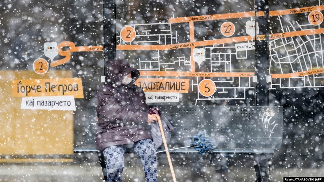 A woman waits for public transport at a bus stop during heavy snowfall in Skopje on April 1.